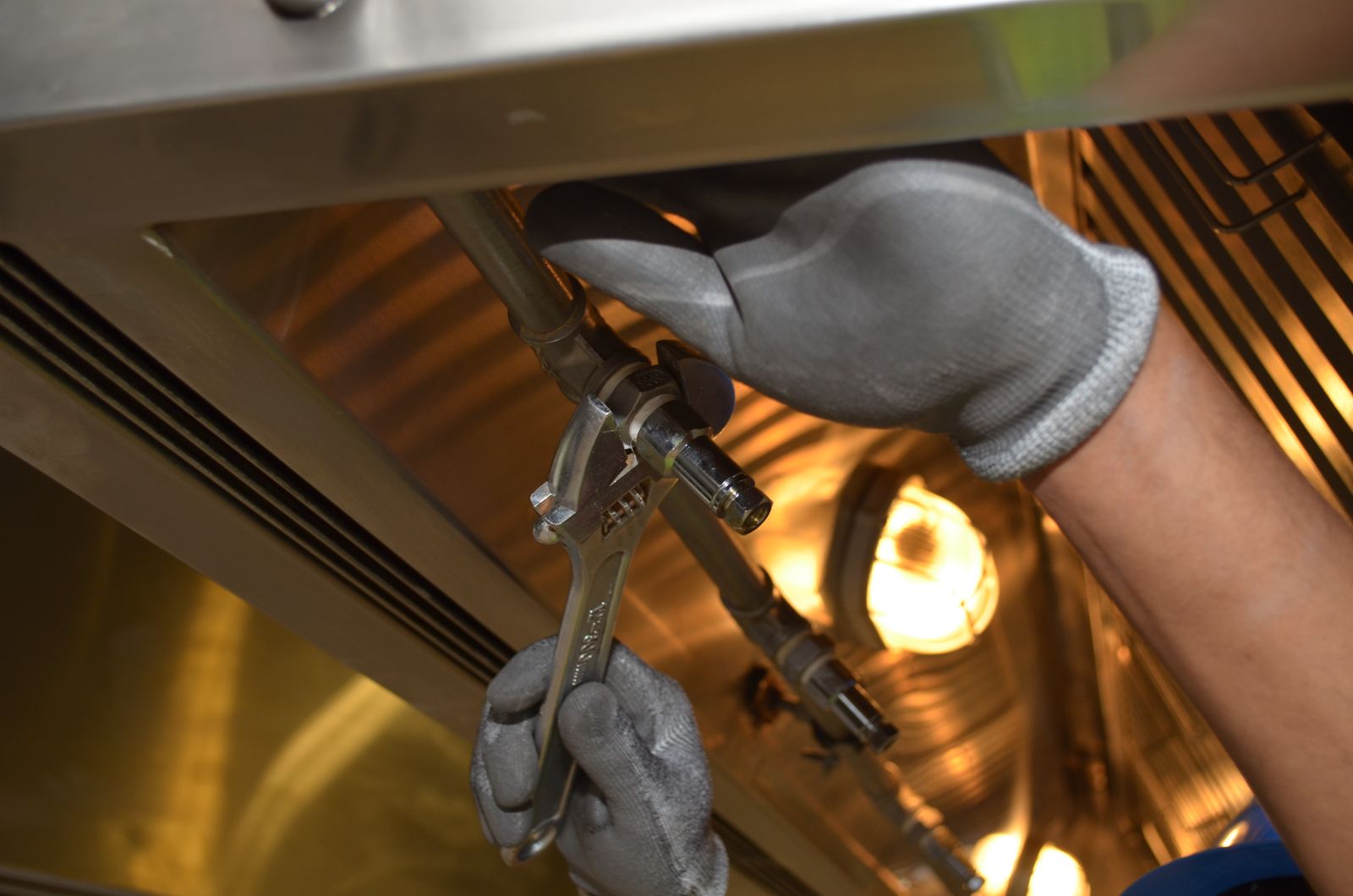Gloved hands tightening a metal pipe fitting